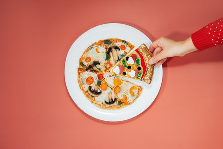 Merry Christmas food offers. Top view hand takes a fake pizza slice on the white plate with veggie...