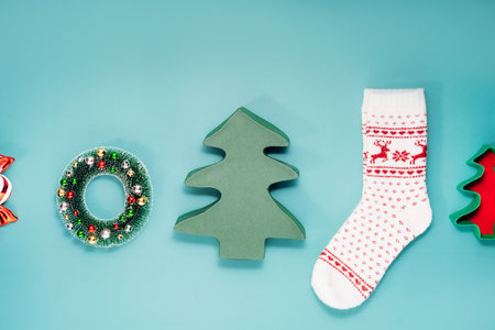 Minimalist Christmas mood concept. Turquoise Background with Christmas attributes as Christmas tree shape gift boxes, warm socks with deer pattern, decorative wreath. Flat lay, top view. Copy space.の写真素材