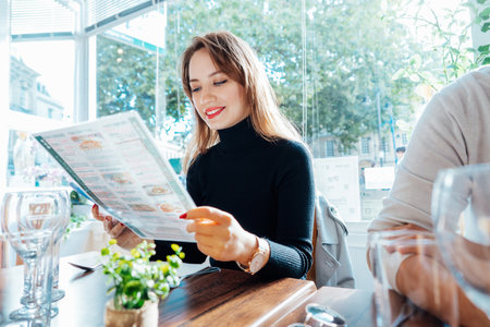 Young woman reading menu sitting with friend at casual cafe. Smiling woman checking menu, choosing meal or drink, making order. Try new foods while traveling. real people. copy space. Selective focus.の写真素材