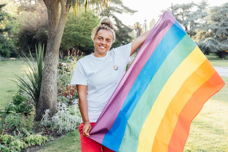 Mixed race woman with a rainbow flag outdoor. Young lesbian activist smiling and holding flag symbol...