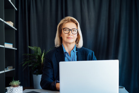 Portrait of smiling 50s stylish, confident mature businesswoman, middle aged company ceo director, experienced senior female professional, business coach working on laptop in office. Female leader.の写真素材