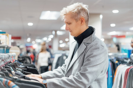 Stylish young man in elegant trendy coat shopping in clothes store. Male customer selecting clothes. Buying clothes in boutique using fitting concept while choosing. Male fashion. selective focus.の写真素材