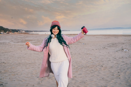 Smiling stylish hipster woman with color hair having fun on the beach, running and dancing on the sand. Happy woman. Off season Travel and freedom concept. Seasonal street fashion. Simple pleasuresの写真素材