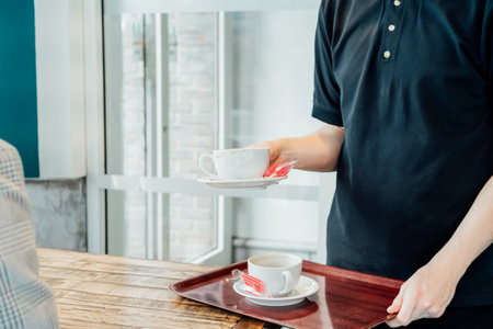 Waiter removing dirty dishes from the tables in cafe. Waiter hand pick up dirty coffee cups. Service job in cafes. Occupation and work concept. Part-time work for youth. Problems of unemploymentの写真素材
