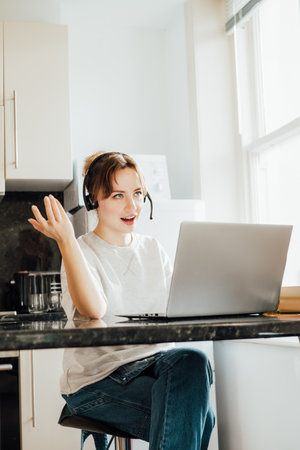 Remote work at home. Emotional Woman in headset working on Laptop at Kitchen Table in flat. Student...
