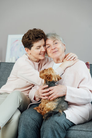 Portrait of happy senior 70s mother, adult neutral gender daughter and Yorkshire terriers dog hugging. Happy family enjoying weekend together in living room. Spending quality time in retiring houseの写真素材