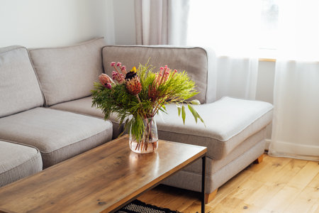 Vase with exotic protea flowers bouquet on coffee table with blurred background of modern cozy light...