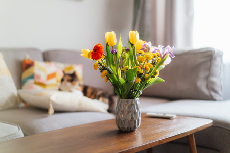 Vase of multicolor flowers on coffee table with blurred background of modern cozy living room with...