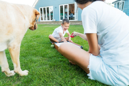 Joyful little boy and his mother are playing portable air hockey in the garden. Fun Playing Games in Backyard Lawn on Summer Day. Happy family time with pet together. Solo parenting. Active childhood.の写真素材