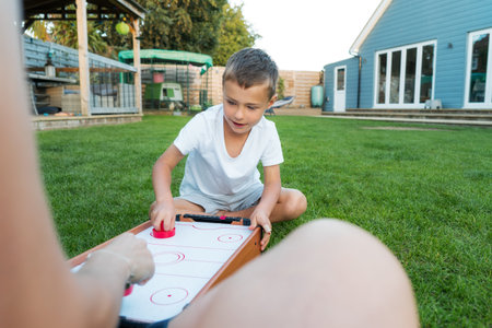 Joyful little boy playing portable air hockey with his mom in the garden. Fun Playing Games in Backyard Lawn on Summer Day. Happy family time together. Solo parenting. Active childhoodの写真素材