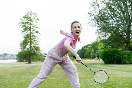 Young excited focused woman with racket playing badminton outdoors in urban city park. Friends having fun outdoors. Enjoying game and natural environment. Adult Outdoor activity. Healthy lifestyle.の写真素材