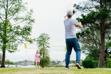 Focus om man with racket playing badminton with young woman in the park. Friends having fun and...