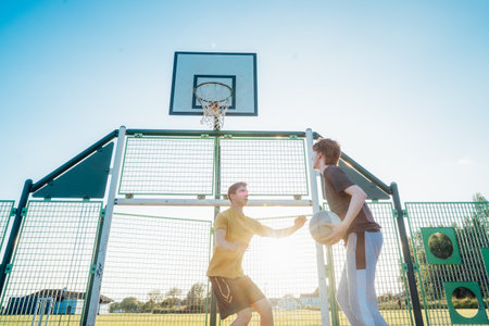 Two Young Caucasian Men Playing Basketball at the Park outdoor playground in sunset light. Teenagers hobby, offline activity. Concept of sports, hobbies and healthy lifestyle. Selective focus.の写真素材