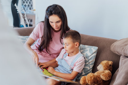 Young Mother and her preschooler son on the sofa reading book for children at home. Studying and playing together at home. Happy childhood and motherhood concept. Selective focus.の写真素材
