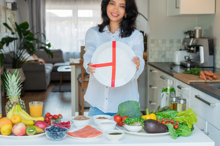 Indian Nutritionist explaining healthy balanced plate according to proportions of nutrients in front of kitchen table with fruits and vegetables. Healthy diet habits, wellness lifestyle, weight lossの写真素材