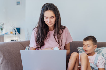 Stressed mother talking with pediatrician doctor during online video chat on pc, worried about her sons health, checking childs temperature by holding hand on kid forehead. Telemedicine, telehealth.の写真素材