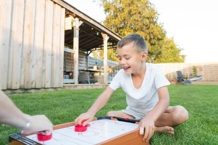 Joyful emotional little boy playing portable air hockey with his mom in the garden. Fun Playing...