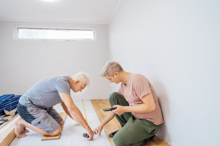 Father and adult son installing flooring in new Home by their own. Doing measurements, calculating...