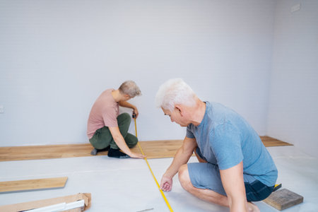 Father and adult son installing flooring in new Home by their own. Doing measurements, calculating for vinyl laminate and skirting. DIY, Do it yourself. Home renovation, improvement, refurbishmentの写真素材