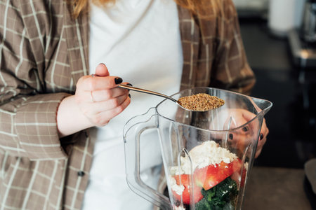 Close up woman adding flex seeds during making smoothie on the kitchen. Superfood supplement. Healthy detox vegan diet. Healthy dieting eating, weight loss program. Selective focus. Copy spaceの写真素材