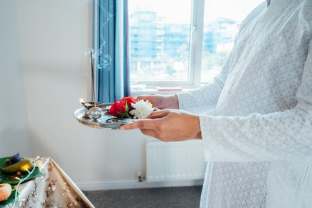 Close up Indian man holding pooja ki thali engages in worship at home altar, adorned with decors and offerings for god Ganesh during festive celebration. Indian culture, hindu ritual and customs.の写真素材