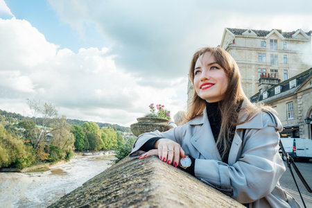 Portrait of Young Woman enjoying sunny day and view of bay with river in picturesque location of Bath city, England. Holiday, travel walk in old European city. Local travel, Sightseeing trip concept.の写真素材