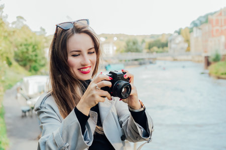Smiling young woman holding retro style camera. Female traveller watching photos on camera during...