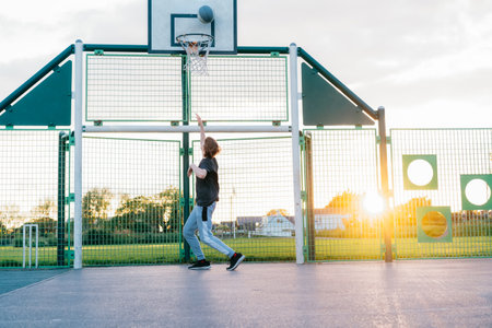 Young Man with basketball ball under hoop, Playing Basketball at Park outdoor playground in sunset...