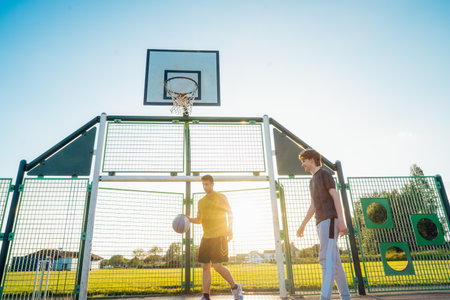 Two Young Caucasian male teenagers Playing Basketball at Park outdoor playground in sunset light....