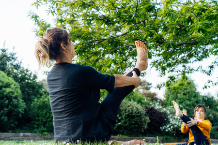 Female yoga class in park. Group of diverse women doing stretching pose exercising together with...
