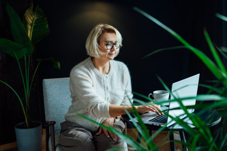 Smiling 50s stylish, confident mature businesswoman, middle aged experienced senior female professional, business coach, mentor, therapist, counselor working on laptop in office. Female leader.の写真素材