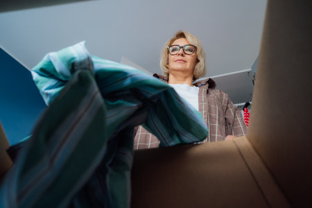 Woman putting selected clothes from her wardrobe for donating to a Charity shop. Decluttering,...