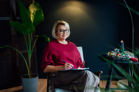 Woman drawing work-life balance wheel sitting on armchair at cozy dark home interior. Self-reflection and life planning for next new year. Personal Year review. Coaching tools. Finding Balance in Lifeの写真素材