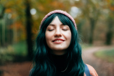 Portrait of young smiling woman with closed eyes enjoying the moment of calm and freedom in autumn forest with fall yellow leaves. Feeling harmony, reunion with nature. Relaxing, mental recovery.の写真素材