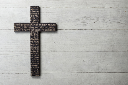 Dark wooden cross with carved the Lords Prayer on worn white wooden backgroundの写真素材