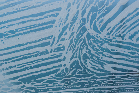Soap foam pattern and bubbles on glass. Blue background.
