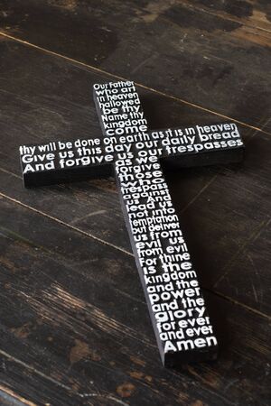 Black wooden cross with  white the Lord's prayer  on the shabby  dark wooden  plank close-up.