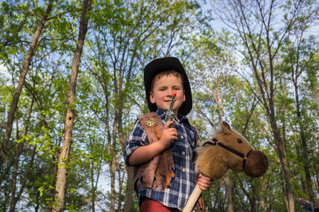 Portrait a little boy dressed like a cowboy with toy horse and pistol on outdoors. Costume partyの写真素材