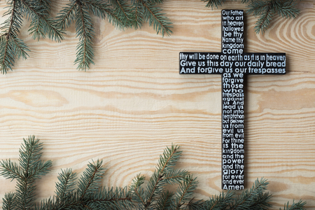Black wooden cross with the Lords prayer on the shabby wooden plank with fir tree branches...