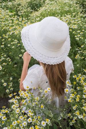 Portrait of a beautiful girl in a white hat and with a bouquet of daisies on a flower meadow backgroundの写真素材