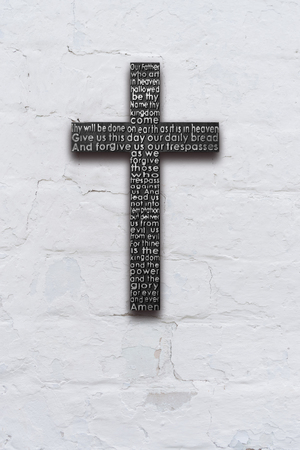 Black wooden cross with the Lords prayer on white  brick wall with shabby stucco backgroundの写真素材
