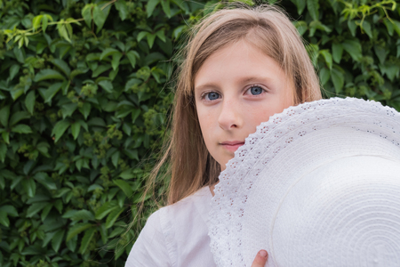 Portrait of a beautiful girl in a white dress and with a hat on a green grape leaf backgroundの写真素材