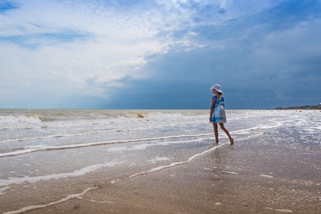 Beautiful seascape. Girl in dress and white hat on the beach over blue sky backgroundの写真素材