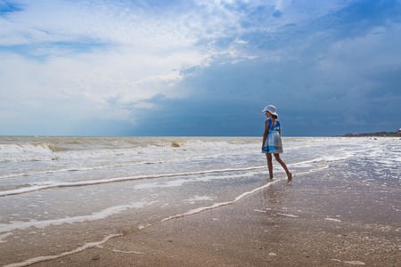 Beautiful seascape. Girl in dress and white hat on the beach over blue sky background