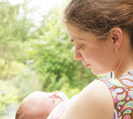 Young mother is by the window with the sleeping baby on hands の写真素材