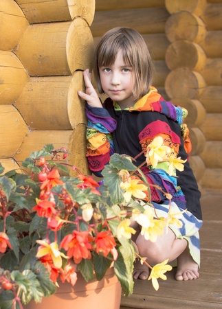The girl is photographed on a balcony of the wooden house with flowers of a begonia の写真素材