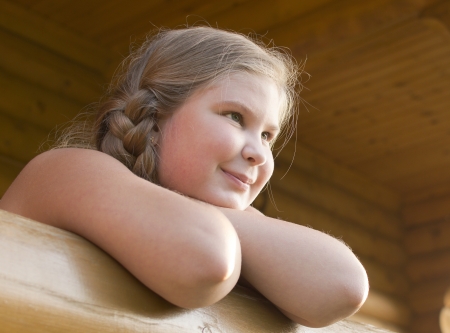The girl is photographed on a balcony of the wooden house の写真素材