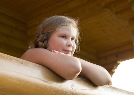 The girl is photographed on a balcony of the wooden house の写真素材