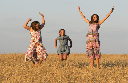 Three joyful girls is jumping in oat field.の写真素材
