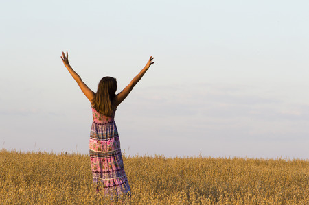 The girl put hands up standing in oat field.の写真素材